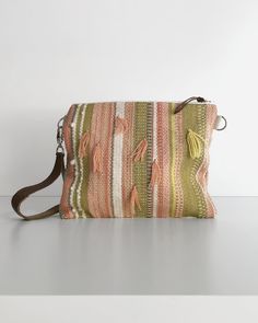 an orange and green striped purse with tassels on the front, sitting on a white surface