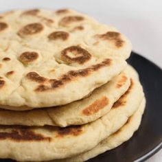 four flat breads are stacked on a black plate