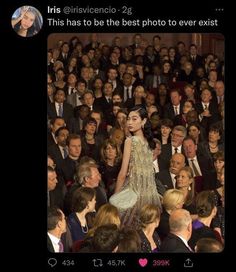 a woman standing in front of a crowd of people wearing formal clothes and looking at the camera