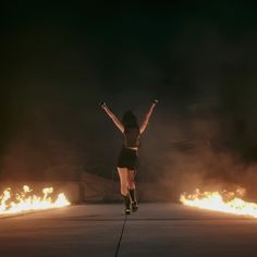 a woman is jumping in the air with her arms up and legs spread wide as fire burns behind her