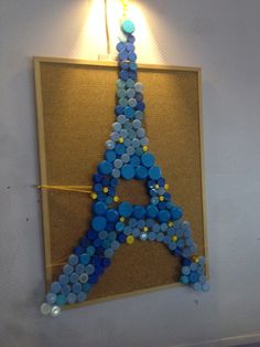 the eiffel tower made out of buttons is hanging on the wall next to a lamp