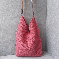 a pink crocheted bag hanging on the wall next to a gray couch with a brown leather handle