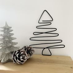 a metal christmas tree next to a pine cone on a wooden table in front of a white wall