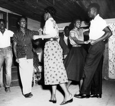 an old black and white photo of some people dancing in a room with other people