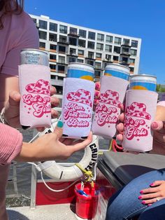 four people holding up pink and white can coolers