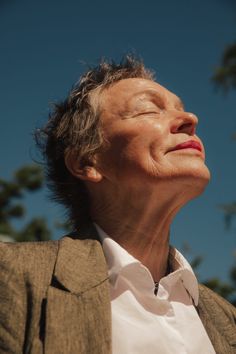 an older woman with her eyes closed looking up at the sky and trees in the background