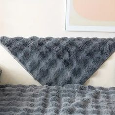 a bed with a gray blanket on top of it and a teddy bear sitting next to it