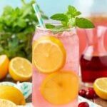 two glasses filled with lemonade and cranberry punch on a table next to fresh fruit