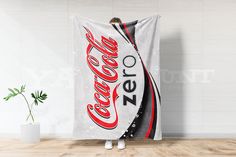 a woman standing in front of a white wall with a coca - cola towel hanging on it