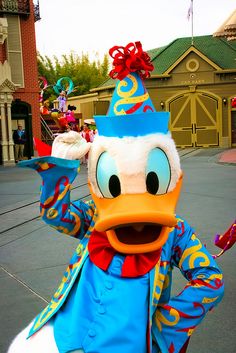 donald duck dressed in blue and yellow with a red bow on his head, waving to the crowd