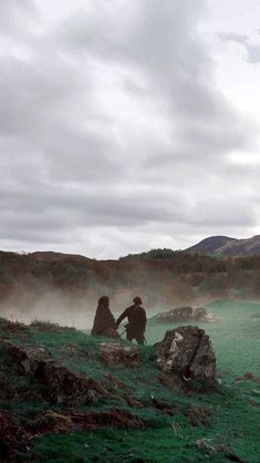 two people sitting on rocks in the middle of a green field with steam rising from them