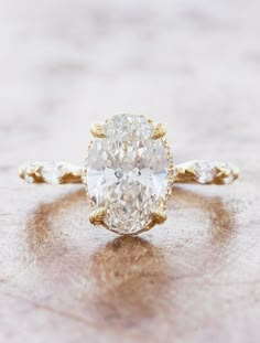 an oval cut diamond ring with three small diamonds on the band, set in 18k yellow gold