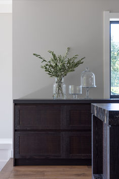 a vase filled with green plants sitting on top of a wooden dresser next to a window