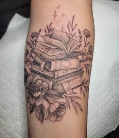 a black and white photo of a tattoo with books on it's arm, surrounded by flowers