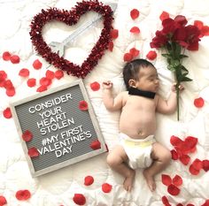 a baby laying on top of a bed next to flowers and a sign that says consider your heart stolen my children valentine's day