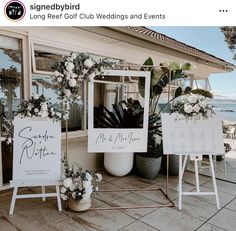 a couple of signs sitting on top of a sidewalk next to flowers and greenery