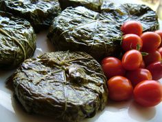 some tomatoes and other food items on a white plate with green leafy wrappers