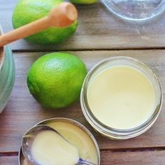 limes are sitting on a wooden table next to two jars with liquid in them