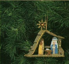 a nativity scene ornament hanging from a christmas tree with green needles and branches