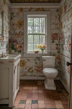 a white toilet sitting in a bathroom next to a window with flowers on the wall