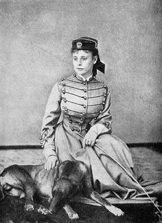 an old black and white photo of a woman in uniform sitting next to a dog