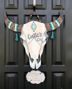 a cow's skull hanging on the front door of a house with turquoise tassels