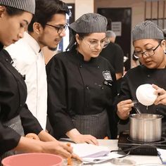 three chefs are preparing food in a kitchen together, one is pouring something into the pot