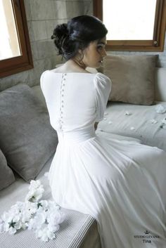 a woman in a white dress is sitting on a couch with flowers around her neck