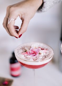 a close up of a person holding a drink in a glass with flowers on it