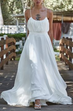 a woman in a white dress is standing on a wooden bridge and looking at the camera