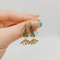 a person holding onto some gold earrings with green leaves on them and a blue nail polish