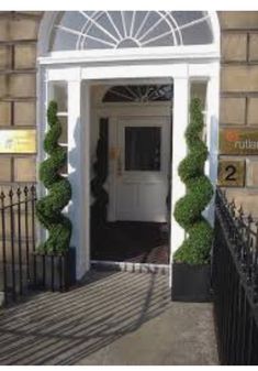 an entrance to a building with two topiary bushes on either side of the door