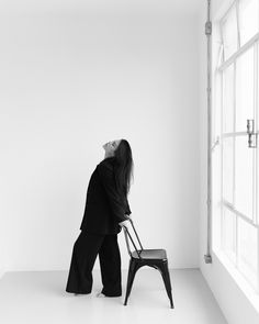 a woman standing next to a chair in front of a window looking up at the sky