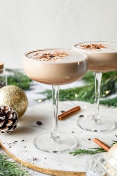 two glasses filled with drink sitting on top of a table next to pine cones and christmas decorations