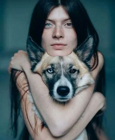 a woman is holding a dog with her arms around her neck and looking at the camera