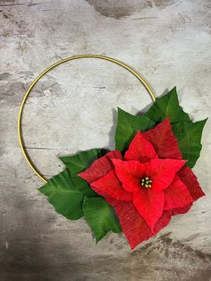 a red poinsettia flower on a gold hoop with green leaves around it