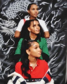 three young women sitting on top of each other in front of a dragon wallpaper