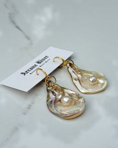 Capture the essence of the sea with these natural oyster shell earrings. Each pair is a unique testament to coastal beauty, showcasing the organic shapes of the ocean. Adorned with semi-precious natural freshwater pearls and delicately crafted with 18k/24k gold and UV resin. Embrace the elegance of simplicity and let your accessories reflect the beauty of the natural world. Shells vary in size making sets 2-3 inches in height. *Each item is quality inspected before being sent out. Please be awar Oyster Earrings, Elegant Teardrop Shell Jewelry, Ocean-inspired Pearl Drop Earrings As A Gift, Handmade Shell-shaped Pearl Earrings Gift, Ocean-inspired Shell Pearl Earrings Gift, Ocean-inspired Pearl Drop Earrings, Ocean-inspired Shell Pearl Earrings For Gift, Ocean-inspired Shell Earrings For Gifts, Handmade Shell-shaped Pearl Earrings