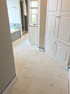 an empty kitchen with white cabinets and marble flooring in the middle of the room