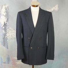 "This navy blue double-breasted blazer has notch lapels and padded shoulders, and closes in the front with one button (four in total show on the front). Three buttons decorate each sleeve cuff. The dark blue wool-blend jacket has three pockets on the front, and is fully lined in a navy blue satin viscose fabric (with two inner pockets). The fabric has a double pinstripe pattern, with a textured chevron herringbone running vertically as well. Brand label: Turo (Made in Finland) Size: 40 US/UK Mat Striped Formal Outerwear With Buttons, Formal Striped Outerwear With Buttons, Striped Formal Outerwear For Spring, Formal Striped Outerwear For Spring, Spring Formal Striped Outerwear, Striped Long Sleeve Sport Coat For Formal Occasions, Striped Double-breasted Suits For Office, Pinstripe Double Breasted Suit For Work, Pinstripe Double Breasted Suit With Long Sleeves For Work