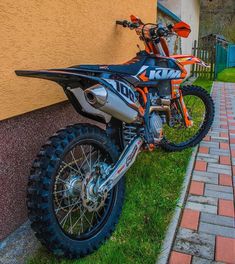 an orange and black dirt bike parked next to a building on the side of a road