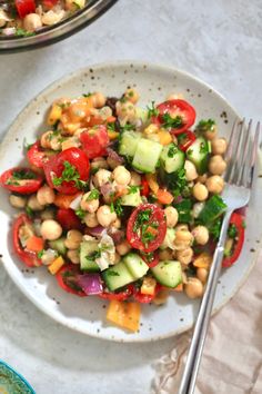 a white plate topped with a salad next to a bowl filled with tomatoes and cucumbers