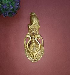 an ornate brass door knockle with a bird on it's head and purple flowers in the background