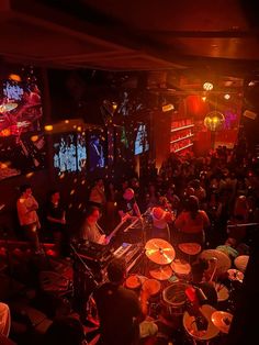 a group of people are playing drums in a room with red and yellow lights on the walls