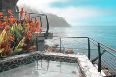 an outdoor hot tub next to the ocean with flowers growing on it's sides