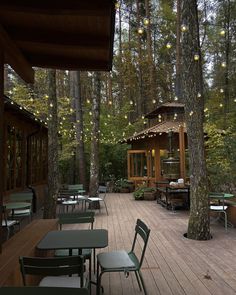 tables and chairs on a wooden deck in the woods with string lights hanging from trees