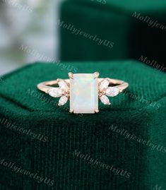 a white opal and diamond ring sitting on top of a green velvet box