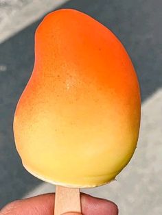 a hand holding an orange and yellow popsicle