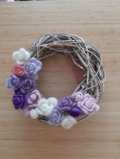 a close up of a wreath on a wooden surface with flowers in the middle and purple, white and pink colors