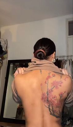 a woman with tattoos on her back standing in front of a mirror